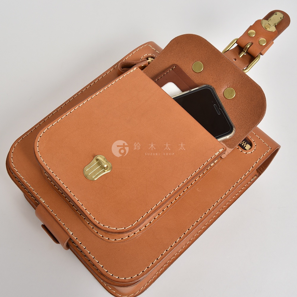 棕色皮革製作的立體口袋兩用單肩包，以白色縫線手工縫製，包蓋上有金色金屬鎖扣，內部可放置手機。