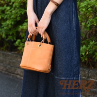 簡約焦糖色皮革手提午餐袋，大開口設計，配有皮革加厚提把及金屬孔眼。袋身有職人縫線裝飾。