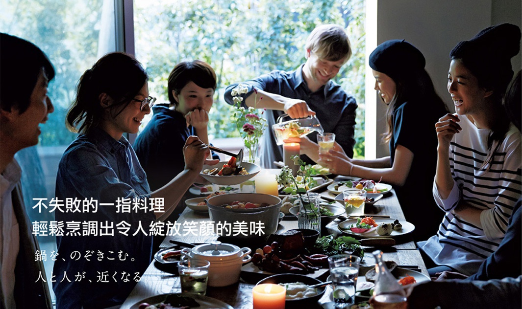 桌上擺滿精緻料理，人們圍坐用餐，氣氛溫馨。其中可見一個淺灰色琺瑯鑄鐵鍋，鍋蓋打開，裡面盛有燉煮的食物。