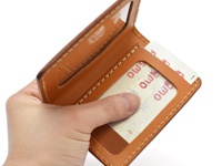 一隻手拿著一個淺棕色皮革雙折票券收納夾，夾內有兩張票券，其中一張的局部字樣為「OWS」。收納夾縫線清晰，材質為皮革。