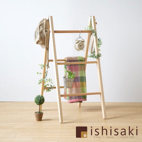 淺色木質梯形牆面收納架，架上掛有卡其色帽子、綠色植物裝飾、復古鬧鐘、格紋毯子及小型盆栽。