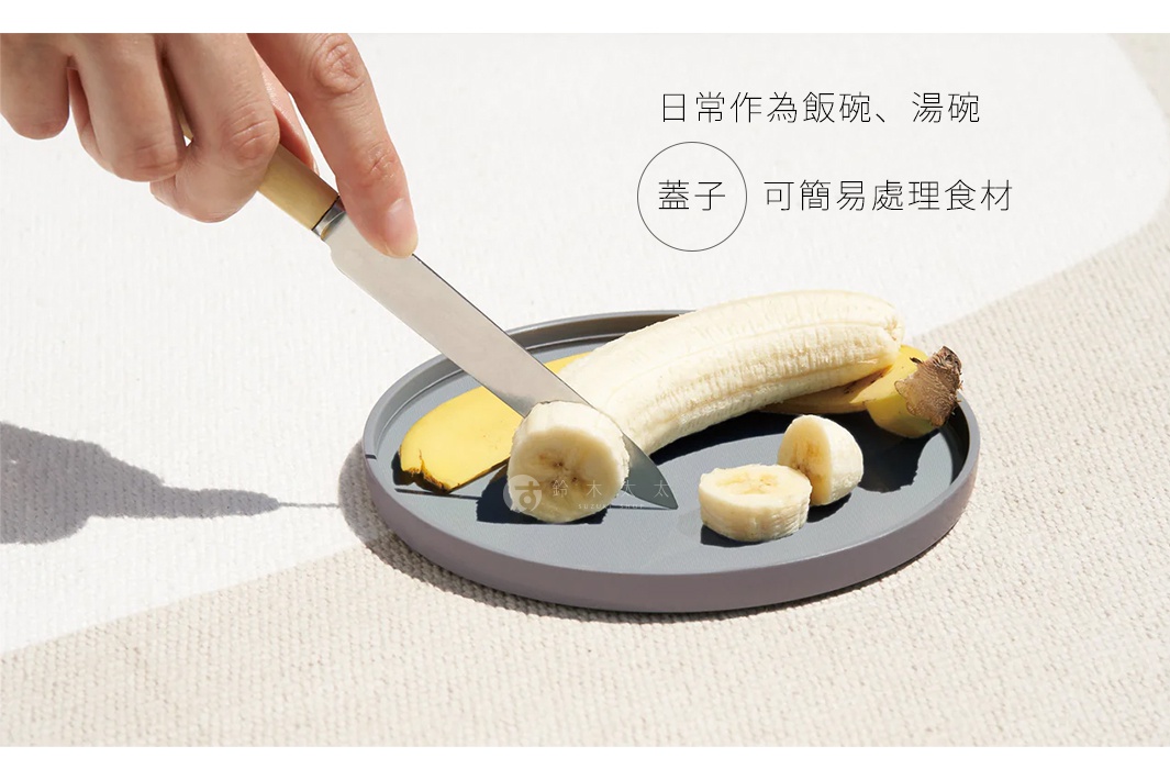 一個灰色圓形餐碗，碗中放著一根去皮的香蕉，香蕉被切成數段，一隻手正拿著刀切香蕉。
