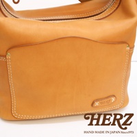 棕褐色厚實皮革單肩波士頓包，正面有弧形翻蓋口袋，白色車線縫製，右下方有品牌壓紋標誌。