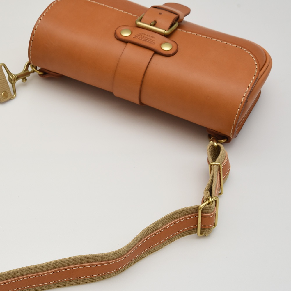 職人手作經典斜背包，採用棕色皮革製作，單扣翻蓋設計，配有可調式帆布織帶與皮革飾邊，以及金色金屬扣環。