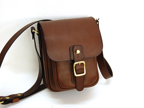 職人手作皮革皮扣直式單肩包，咖啡色皮革製成，有金屬皮扣和可調節式肩帶。
