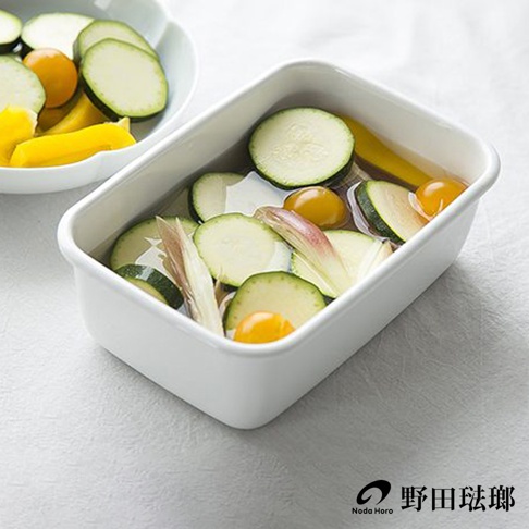 長方型白色琺瑯保存容器中，裝有切片的櫛瓜、小番茄、薑片與黃色甜椒，容器內有液體。
