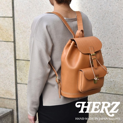 職人手作皮革經典後背包 R-4，採用天然棕色皮革，設有束口主袋、前方翻蓋式小口袋，並以金屬扣環和繩子固定。