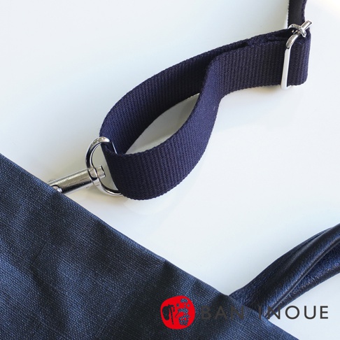 BAN INOUE 品牌標誌旁的釉面亞麻布三用托特包細節，包含深藍色帆布背帶和金屬掛鉤。