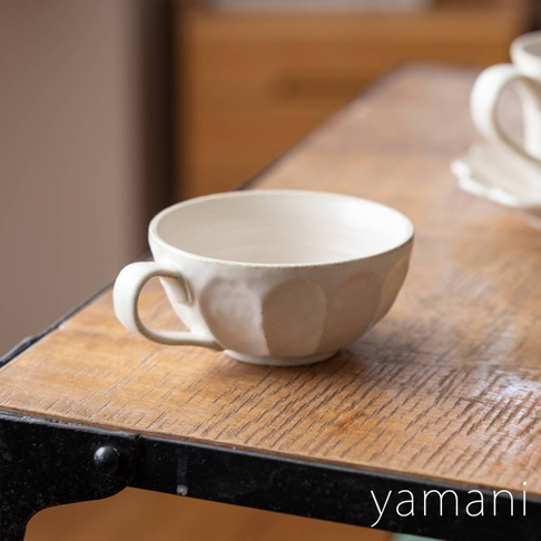 一個米白色、表面帶有六邊形壓紋的陶瓷湯杯碗，有單邊把手，置於木紋桌面上。