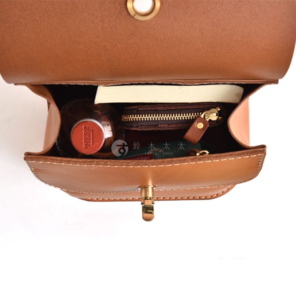 職人手作皮革翻蓋迷你後背包，展示內部空間，裝有書本、錢包和一瓶飲料，皮革顏色為棕色，縫線清晰。