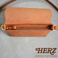 職人手作皮革隨身斜背包，近距離特寫，展現焦糖色皮革的細緻紋理與縫線，以及金屬拉鍊的質感。