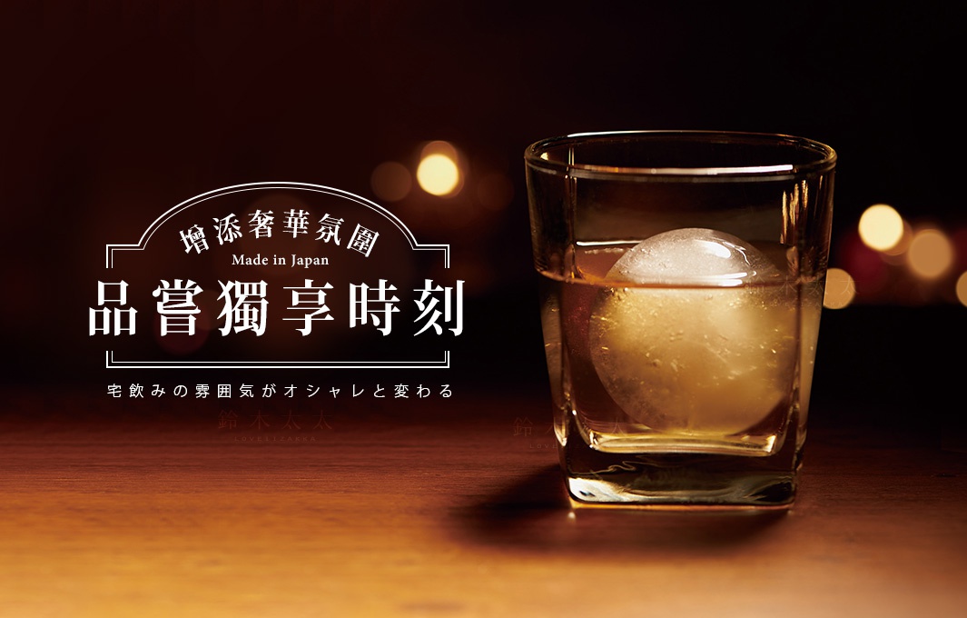 透明玻璃杯盛裝琥珀色液體，杯中置有一顆圓形冰塊。背景為深色調，有模糊的暖色燈光。