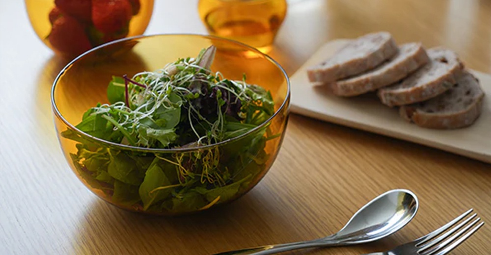 琥珀色透明圓潤點心碗，裝有新鮮沙拉，旁邊有切片麵包、湯匙和叉子。