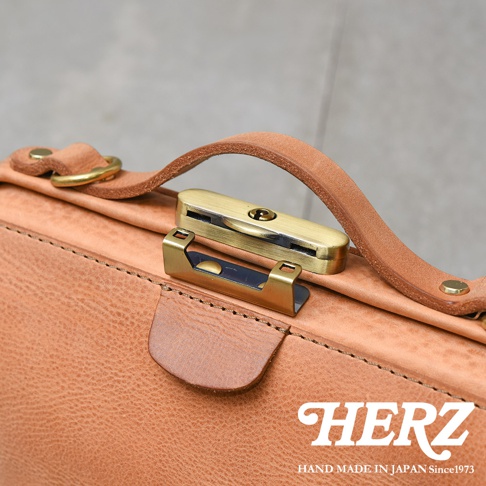 HERZ 職人手作皮革包的特寫，展示了閃亮的鎖孔式金屬扣、皮革提把和縫線細節。