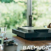 The Plate Pro 極致電烤盤，黑色，擁有簡潔的方形設計，金屬烤盤表面光滑，搭配黑色霧面機身，置於木質桌面，後方為模糊的綠色植物背景。