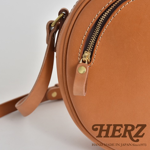 職人手作皮革小圓包，採用溫暖的棕褐色皮革，搭配金色拉鍊與同色系皮革拉頭，簡潔圓潤的設計，展現細緻的車縫工藝。