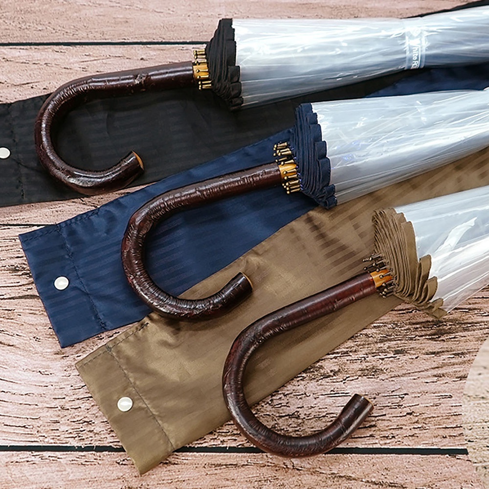 職人高級樺木透明傘，特寫深棕色帶有紋理的彎曲樺木手柄，傘面為透明塑膠材質，傘骨末端與傘布邊緣為深藍色，傘身收納於不同顏色的傘套內，包括黑色、深藍色和淺褐色。