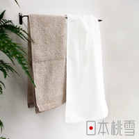 兩條Furry雙股紗絨毛浴巾，一條為淺褐色，另一條為白色，皆懸掛於黑色毛巾架上，背景為白色牆面，左側有綠色植物葉片。