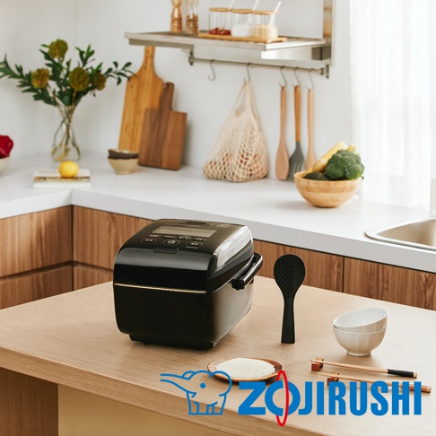 黑色壓力IH電子鍋，帶有銀色飾邊，置於木質檯面上，旁邊有黑色飯勺、白色飯碗及筷子。