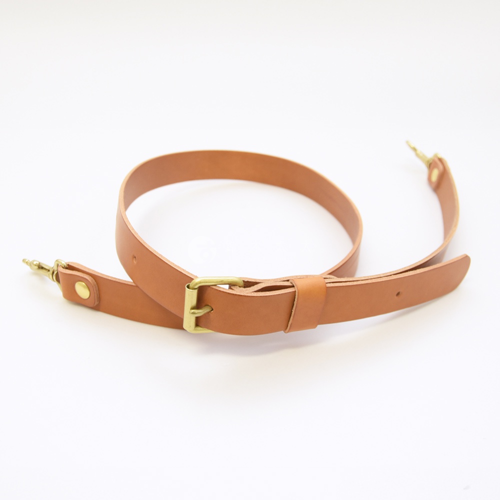 職人手作皮革肩背帶，採用天然棕色皮革，配有黃銅色金屬扣環和掛鉤，可調節長度。
