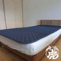 單人床墊鋪設在白色床單上，床墊表面為深藍色菱格紋填充，邊緣有黑色滾邊。床架為木質，床頭板為木條設計。