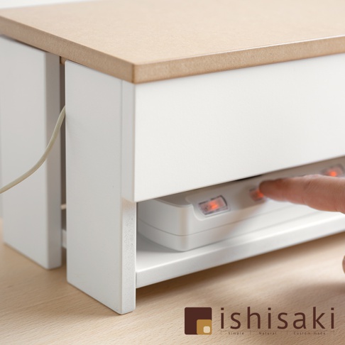 白色木藝附蓋電線收納盒，上方為淺棕色木紋桌面，盒身兩側有開孔，內部可見白色插線板，有橘色指示燈亮起，手指正按下開關。