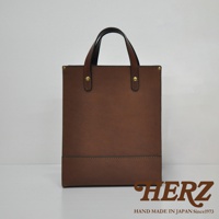 職人手作皮革直式托特包 T-44 M，採用溫潤的棕色皮革，簡約的方形設計，搭配一對皮質提把，提把處以金屬鉚釘固定，包身下方有一條橫向縫線裝飾，整體呈現經典實用的風格。