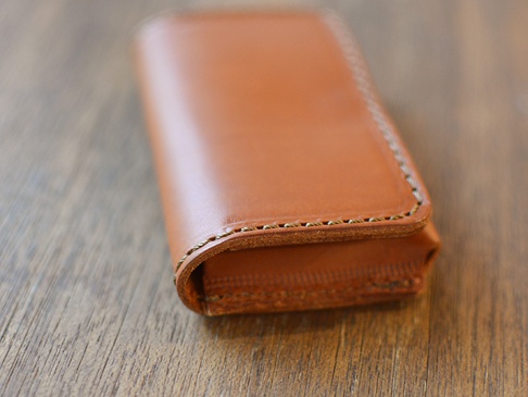 職人手作皮革Organ名片夾，採用棕色牛皮製成，車縫線明顯，風格簡約，置於木紋背景上。