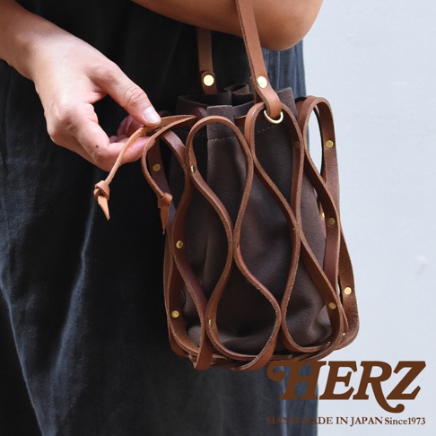 日本HERZ手工皮革編織水桶包，深棕色麂皮內袋搭配編織皮革網架，手部正在調整袋口繫繩。