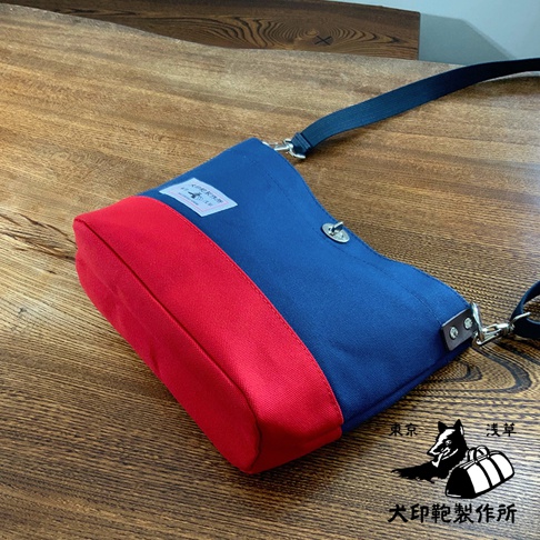 犬印純綿帆布雙色迷你側背包，採用海軍藍與紅色拼接設計，帆布材質，配有可調節式肩帶，整體風格簡約。