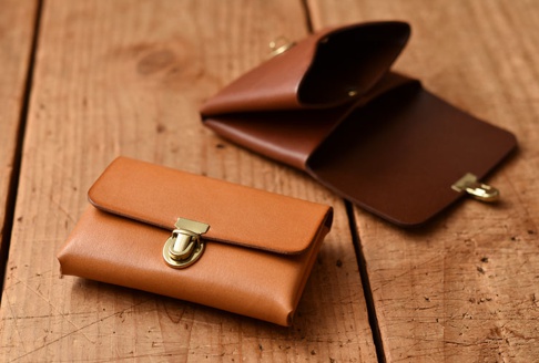 淺棕色皮革卡片夾，配有黃銅鎖扣，旁邊另有一個較深棕色的皮革卡片夾，部分展開。