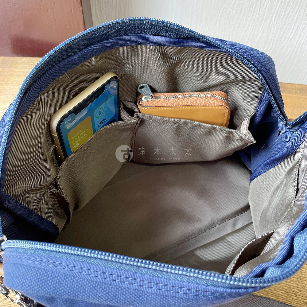 藍色帆布旅行側背包內部，可見手機與皮夾放置於內袋中，包包內部空間寬敞，有分層設計。