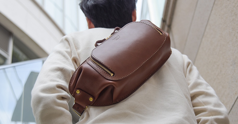 從背部視角看，一個斜背在身著米白色套頭衫的人身上的棕色皮革斜背包。