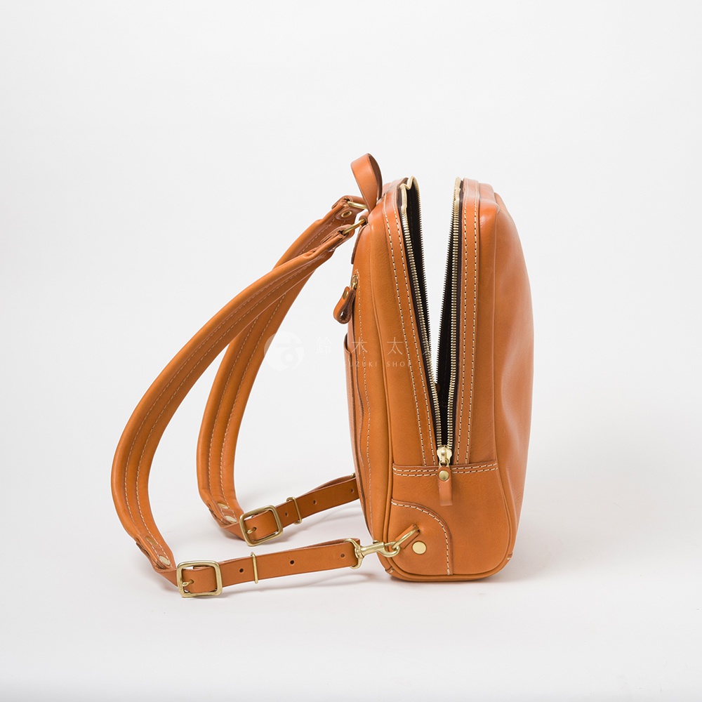 焦糖色皮革製成的商務後背包，側邊視角，拉鍊部分開啟，露出內部，搭配金屬扣環和雙肩帶。