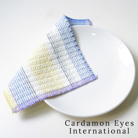 一條由壓克力纖維製成的清潔巾，白色基底搭配藍色、黃色條紋和黑色網格紋，邊緣有紫色縫線。