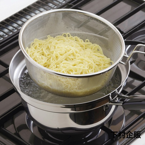 不鏽鋼防溢汆燙鍋，附帶一個細網篩，內盛煮熟的黃色麵條，鍋中裝有冒泡的沸水，置於瓦斯爐上。