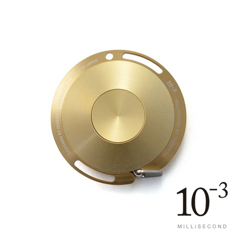 金色鋁製卷尺，圓盤狀外殼，帶有刻字「DESIGNED BY HIDEBUSHI YAMAGUCHI MADE IN JAPAN」、「MILLISECOND BY TAKEDA INC.」及「10-3」。