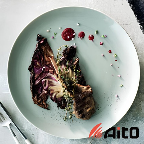 淺藍色圓形餐盤，盤中盛有烤紫甘藍、肉排及迷迭香，盤面點綴著紅醬、香草碎及粉紅色小花，營造精緻的餐點擺盤。