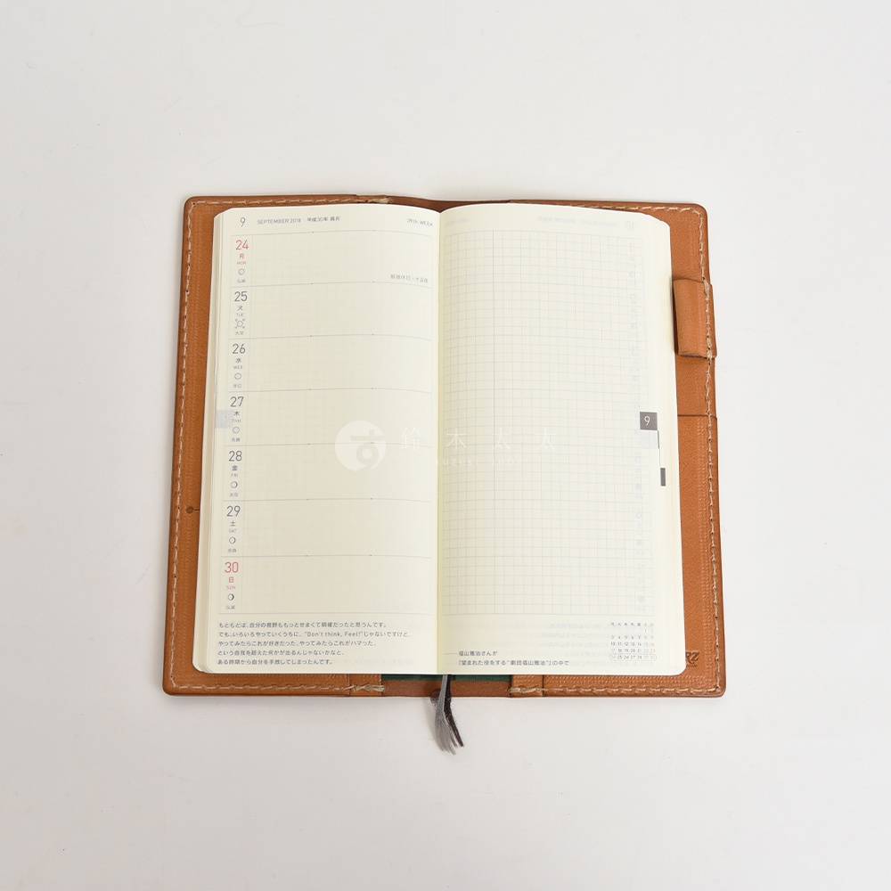 職人手作皮革旅行記事本書套，棕色皮革外殼，內有兩頁式日曆格式筆記本，左頁為每日行程，右頁為網格筆記頁。