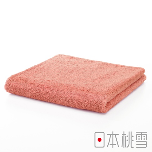 一張珊瑚粉色精梳棉飯店毛巾，折疊平鋪，毛巾表面紋理清晰，材質柔軟蓬鬆。