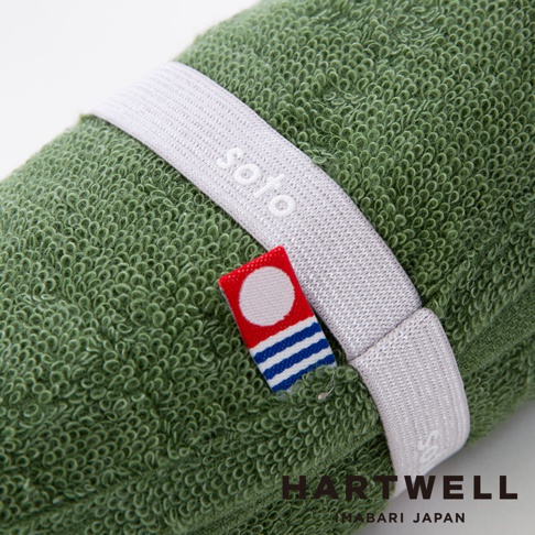 綠色毛巾纏繞著白色束帶，束帶上印有soto字樣，旁邊有一個小標籤，標籤上有紅底白圓點和藍白條紋。