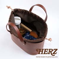 職人手作皮革束口手提包，深棕色皮革，內襯為深棕色帆布，束口處有繩結設計，包內裝有保溫瓶、筆記本、零錢包及藍白花紋布料。