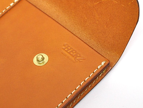 職人手作皮革信封式雙釦手拿袋，採用棕色皮革，附有金色圓形按釦，袋內印有「HERZ」品牌標誌。