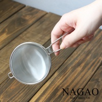 一只手正握著一個不鏽鋼製超細目濾茶器，濾網呈銀色，帶有細密的網孔。