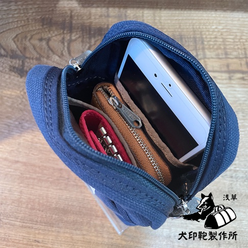 石洗帆布斜背手機包，深藍色，包內裝有白色手機、棕色零錢包和紅色鑰匙圈。