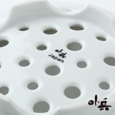 白色美濃燒多用蒸盤，表面佈滿大小不一的圓孔，材質為陶瓷，盤緣有波浪狀設計，盤面上印有黑色日文及「Japan」字樣。