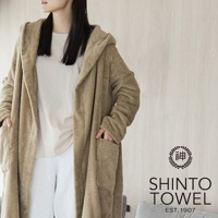 一名女子身穿淺棕色連帽蓬鬆浴袍，浴袍為長袖設計，兩側有口袋，材質看起來柔軟舒適。