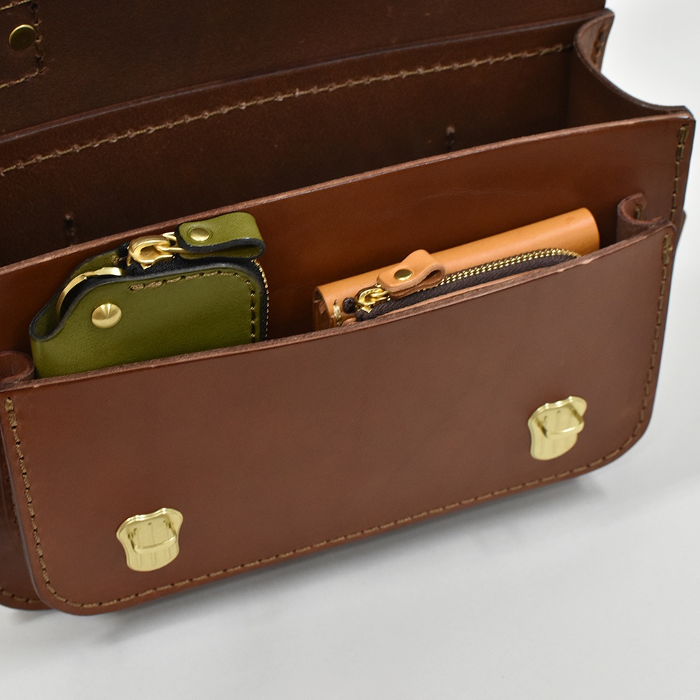 棕色皮革迷你肩背包，內部有綠色與原色皮革零錢包，搭配金色拉鍊與釦環。