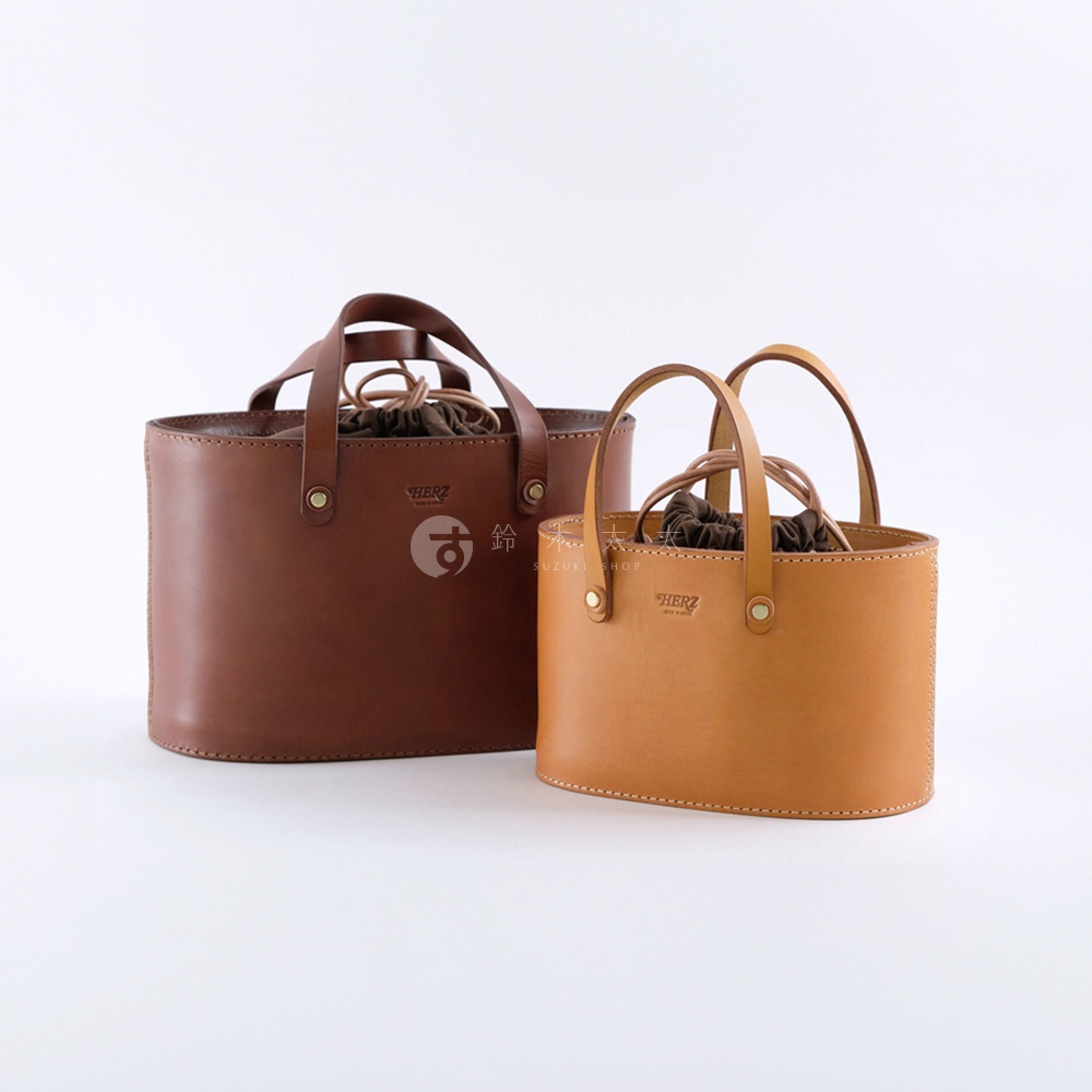 職人手作皮革束口手提包，一深棕色、一淺棕色，兩款包皆為皮革材質，束口設計，配有提把，展示於白色背景。