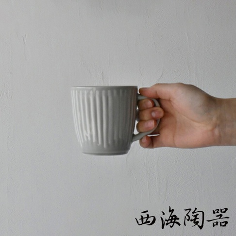 一個灰色陶瓷馬克杯，杯身有垂直凹槽紋路，杯柄為彎曲設計，由一只手持握。